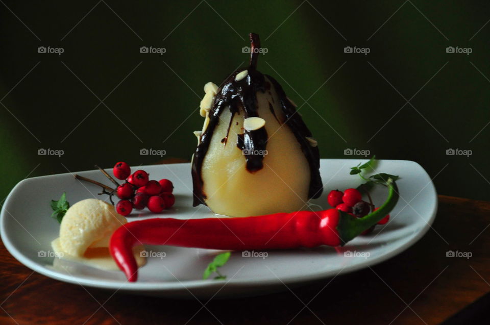 autumn dessert pear with chocolate sauce almonds ice cream and chili on white triangular plate with green background