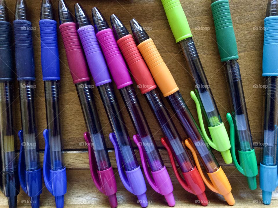 Closeup still life of colored pens. Row of colors in rainbow order on wooden drafting table.