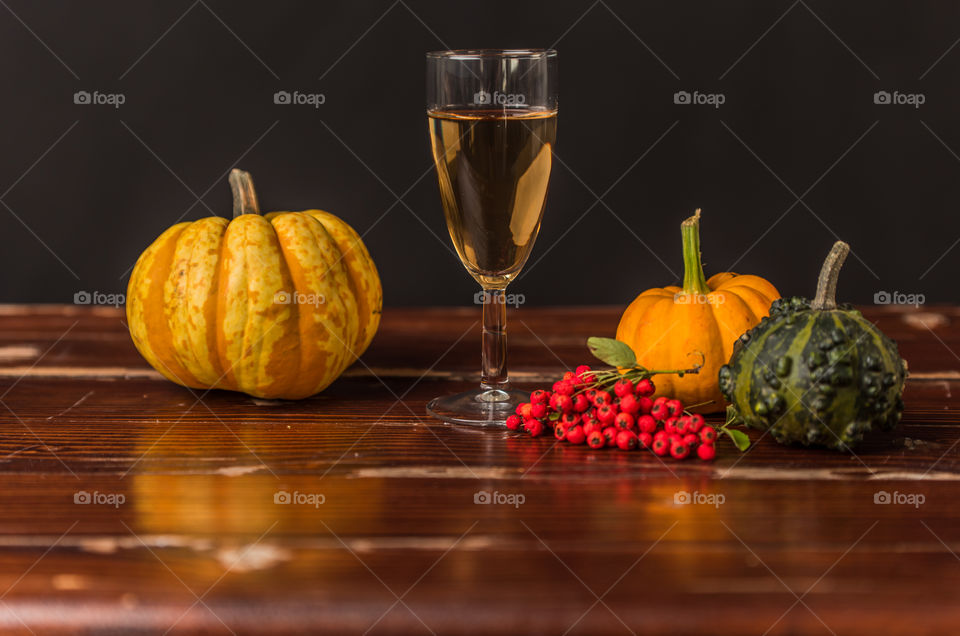a glass of wine on a rustic table, next to pumpkins, leaves and rowan