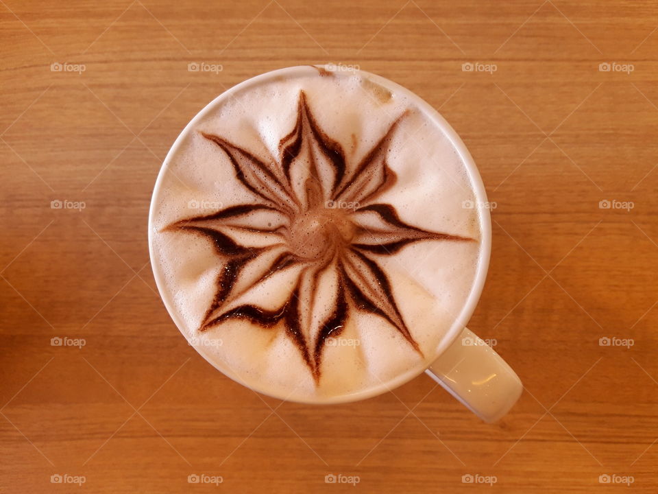 The flower latte art cofee in white cup on wood table