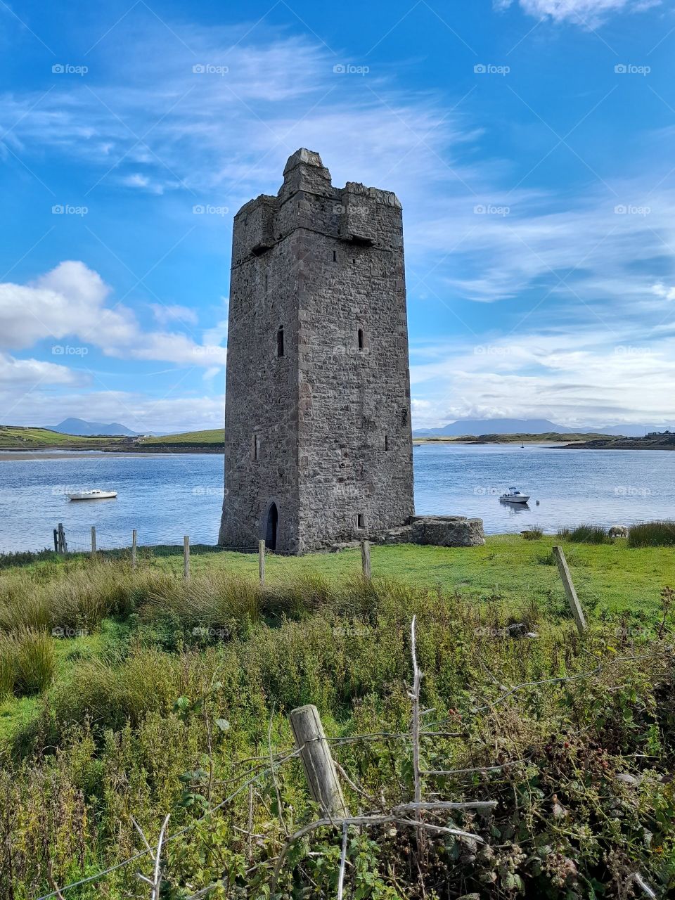 Irish castle, tower house, summer landscapes Ireland at the shoreline with boats passing by, peaceful and tranquil