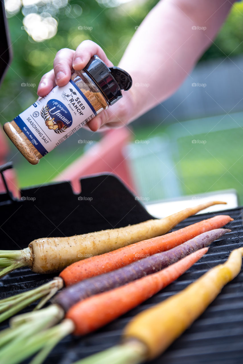 Person shaking Seed Ranch Umami seasoning onto grilled carrots 