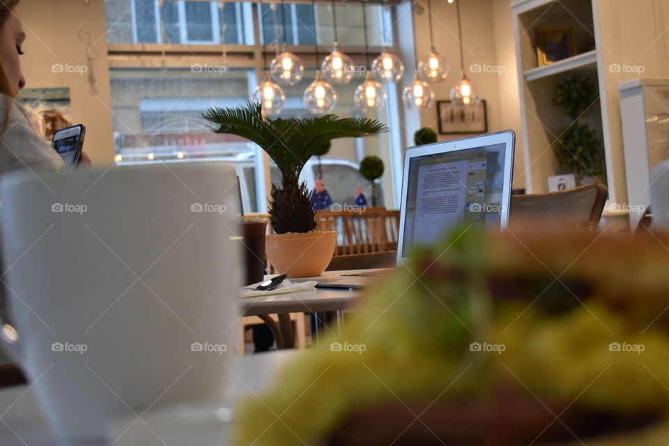 cafe setting. overhead lights. plants on table. computer on table. coffee cup and food.