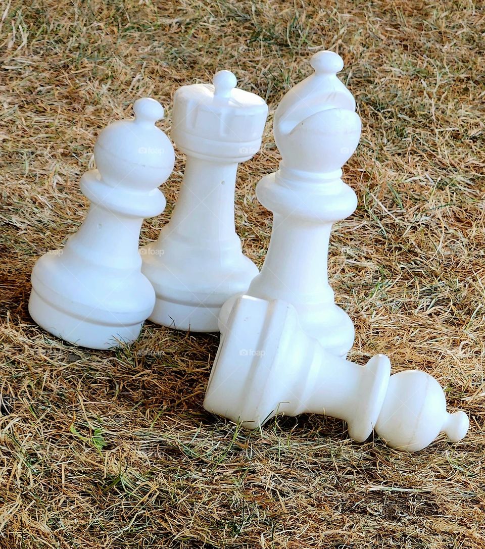 a few large white plastic chess pieces in a grassy field without a game board at an Oregon fair