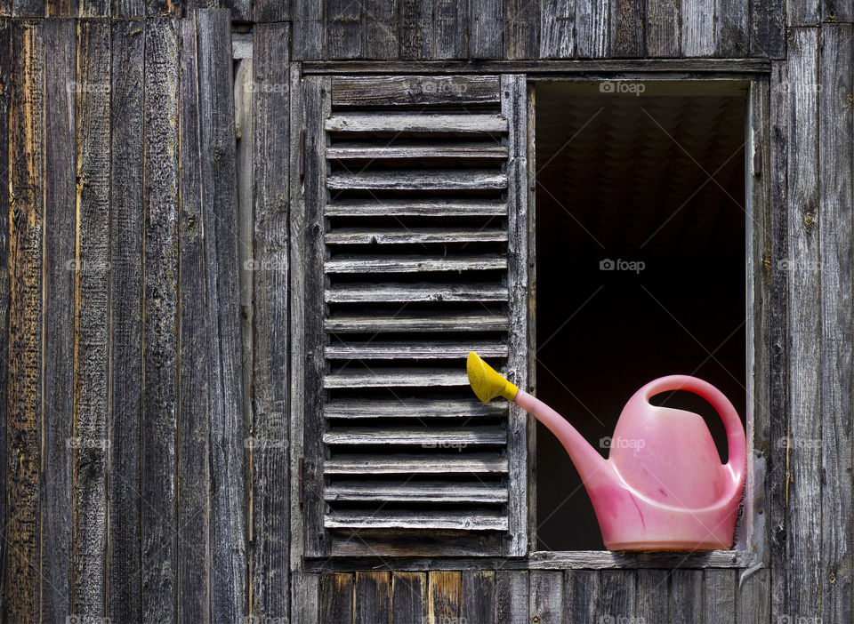 Pink watercan on window of wooden old house