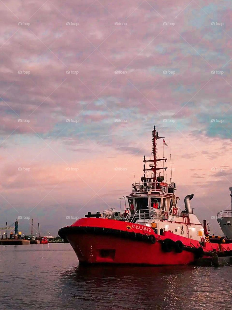 Close-up of a red tugboat anchored in the harbor at sunset or sunrise, with a pink and purple sky in high angle view