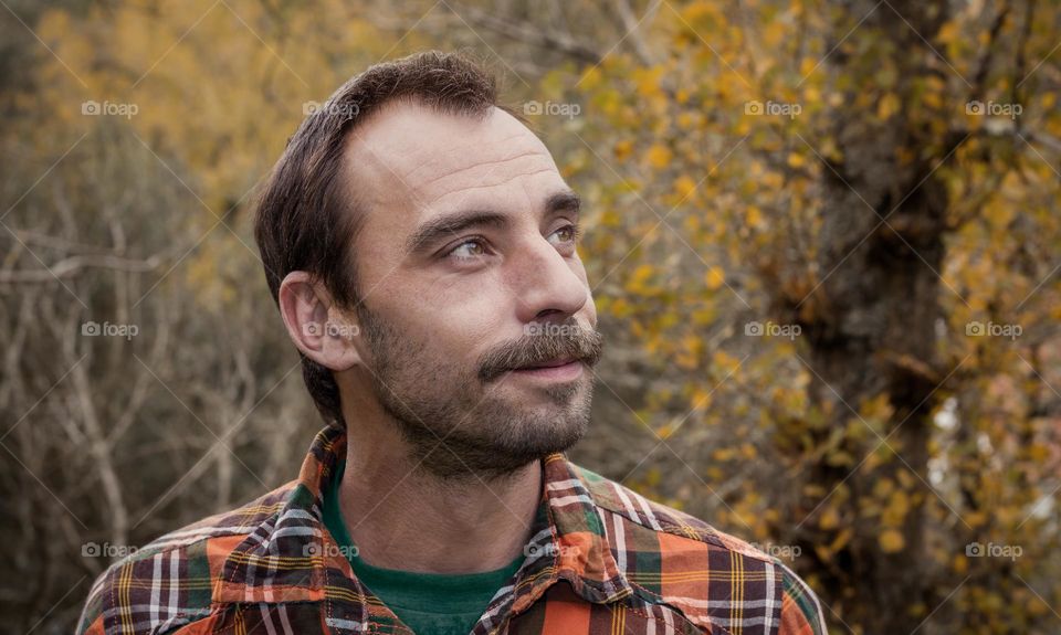 Man in orange plaid shirt, with a background of autumn foliage 