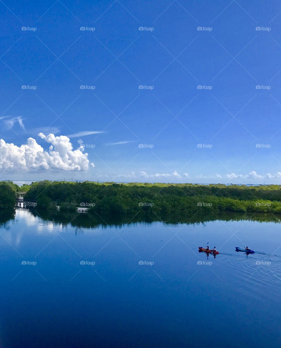 Amazing blue sky and bay water interrupted by two distant kayaks and a grassy island 