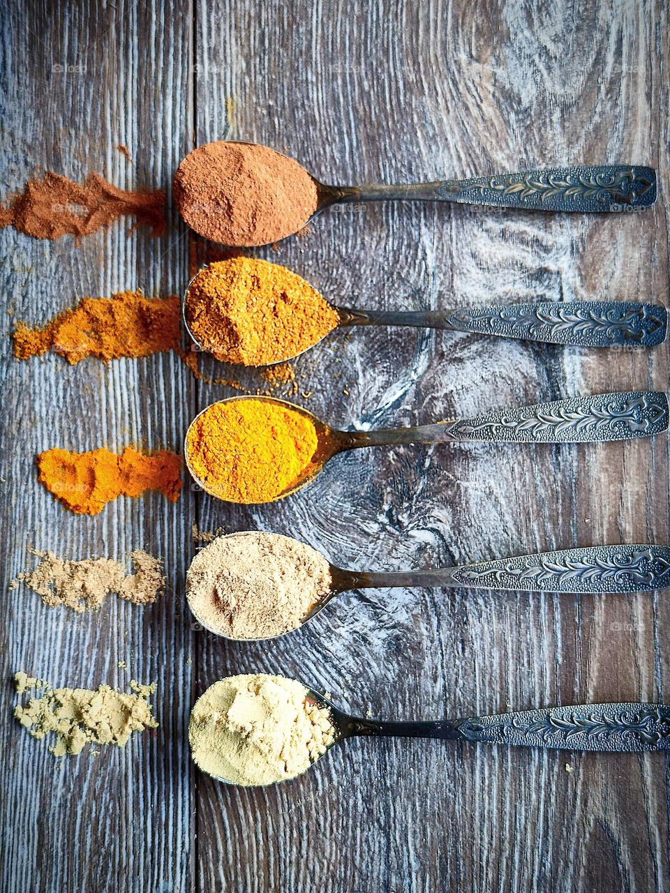 Yellow color. All shades of yellow: from pale yellow to dark yellow. On a wooden background are five spoons with spices: ground ginger, ground mustard, curry, turmeric and ground cinnamon. Spices are scattered around each scoop of a spoon.
