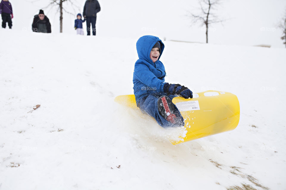 Boy sledding in the snow wearing full winter coat and jacket. 