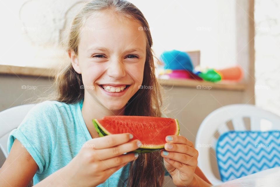 Happy girl sitting in house eating watermelon