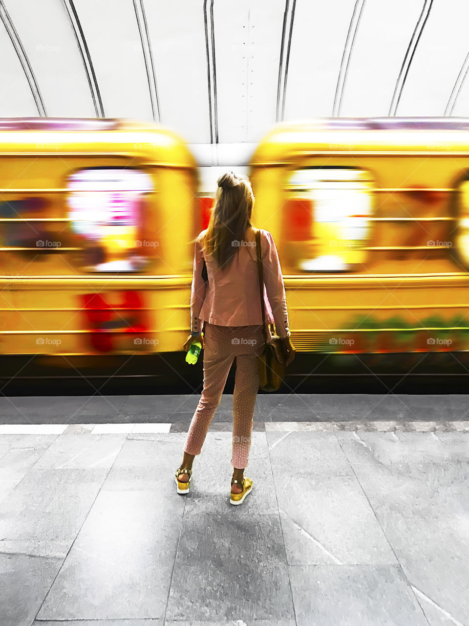 Young woman standing in front of moving yellow subway train 