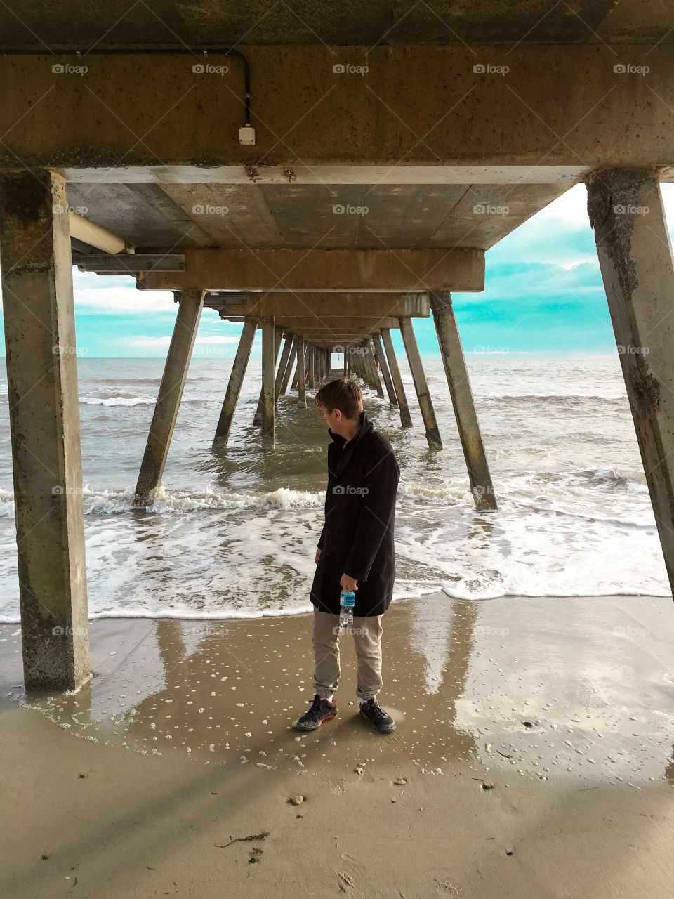 Young man standing under a Jetty looking behind him, 