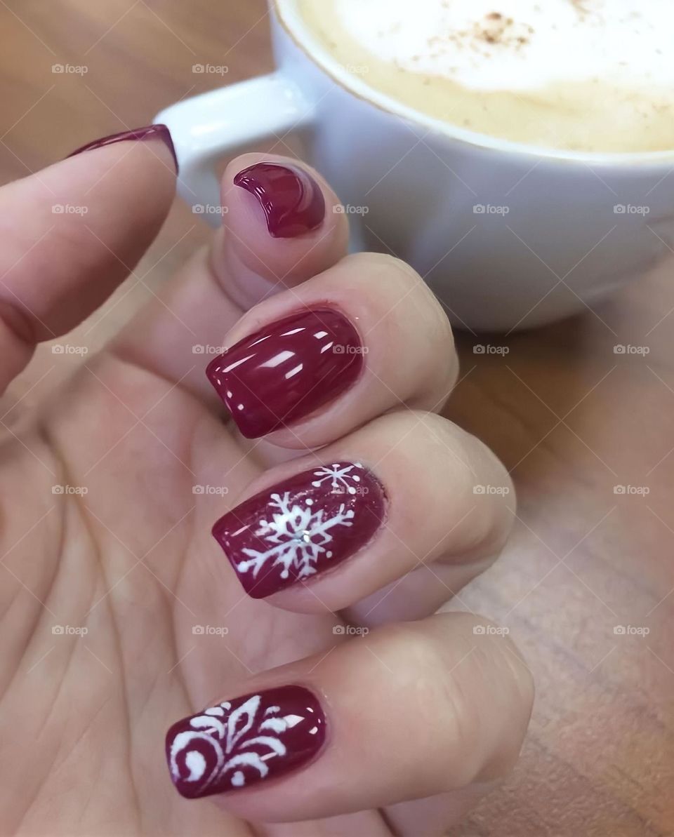 female hands with a beautiful burgundy manicure for the new year and a white snowflake drawing