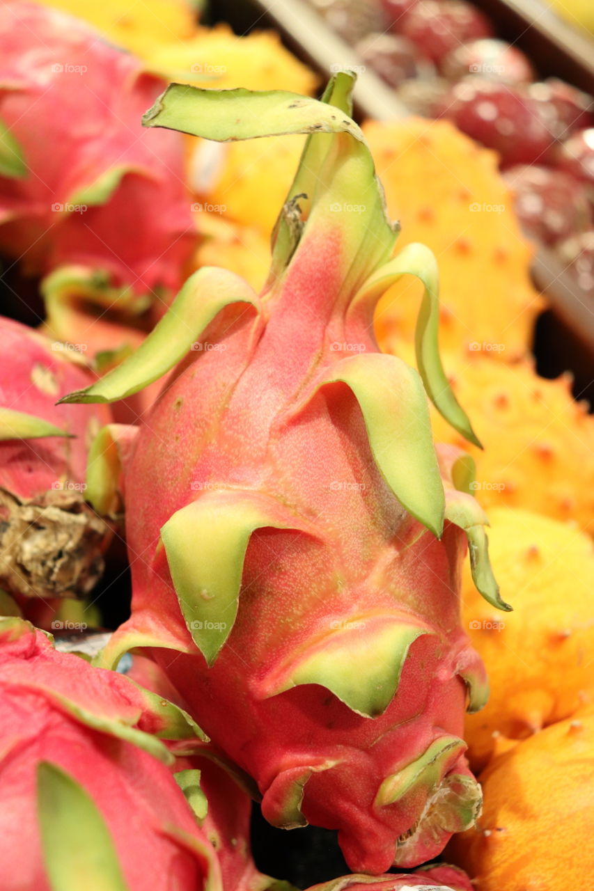 brightly colored dragonfruit with green leaves and orange fruit on the side. 