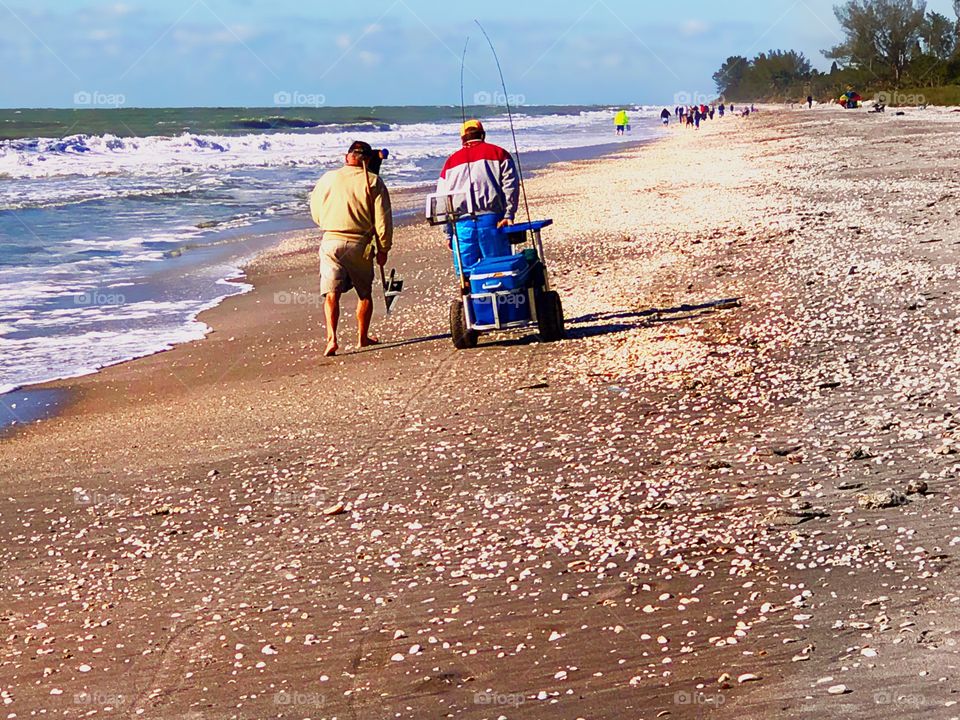 Two beachcombers enjoying their day together shell collecting and pole fishing.