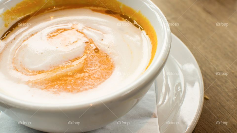 Cream of carrot soup with orange essence oil topped with swirl of crème fraîche ready to eat elevated view on wood table in bowl conceptual healthy eating comfort food