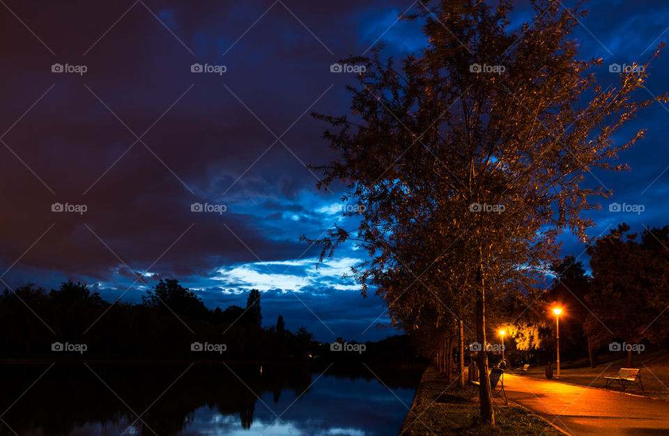 Illuminated street against dramatic sky at night