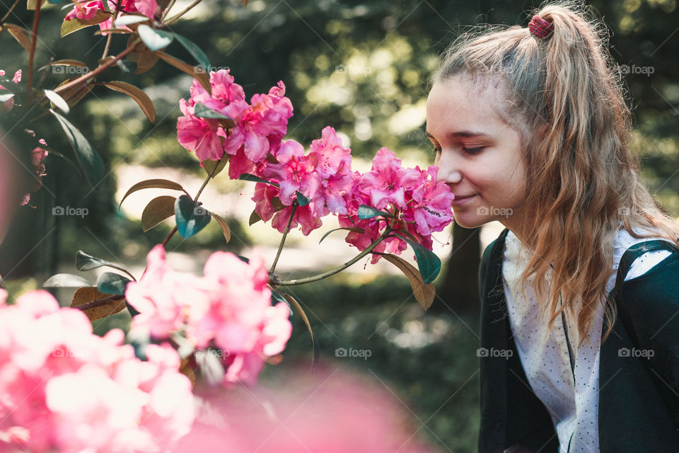 Girl with closed eyes standing in garden among the flowers, smelling beautiful pink flower