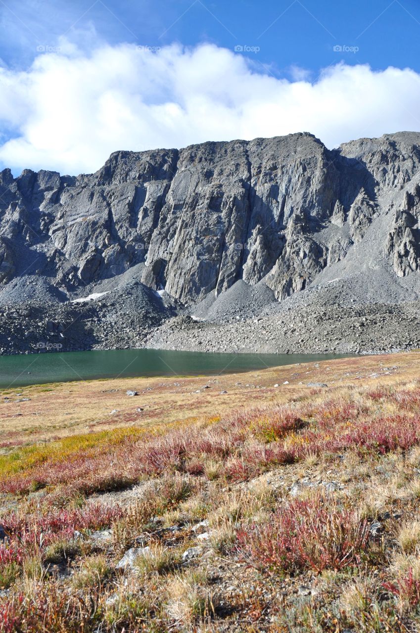 A blue sky and colorful tundra set the stage for an enormous mountain and high alpine lake to shine and delight. Alpine meadow touches the spirit.