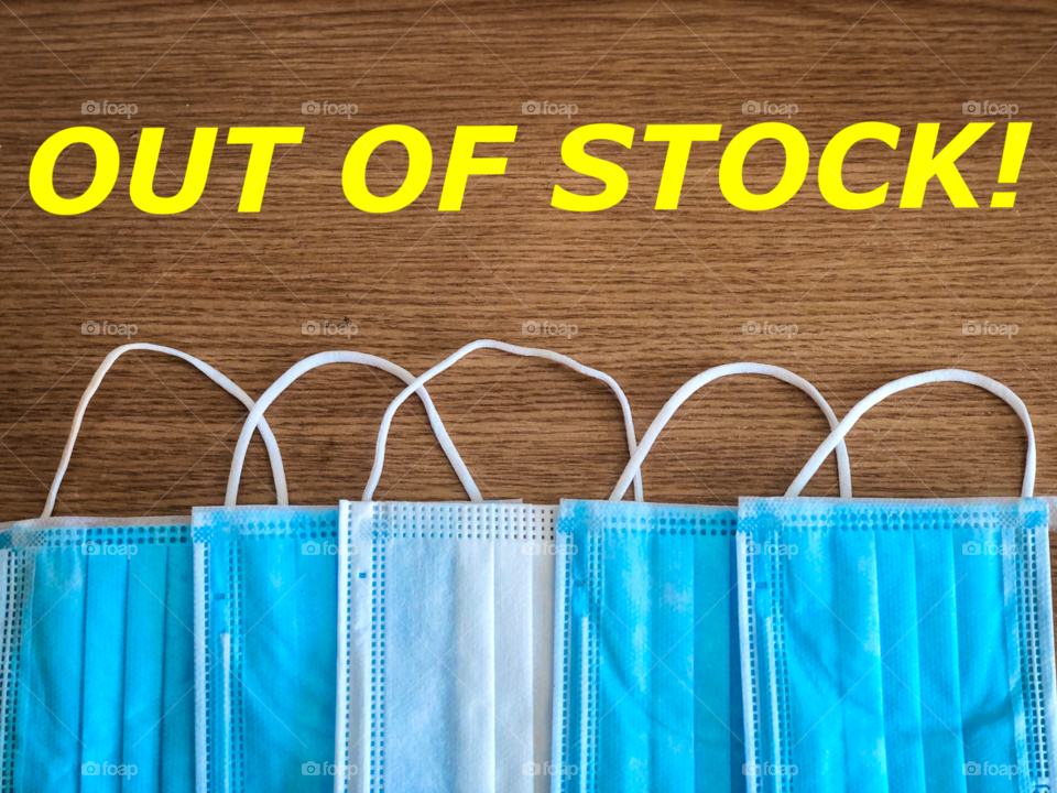 Pile of surgical masks on wooden table with the message “out of stock”
