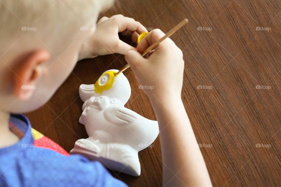 Faceless boy drowning gypsum duck in yellow colour 