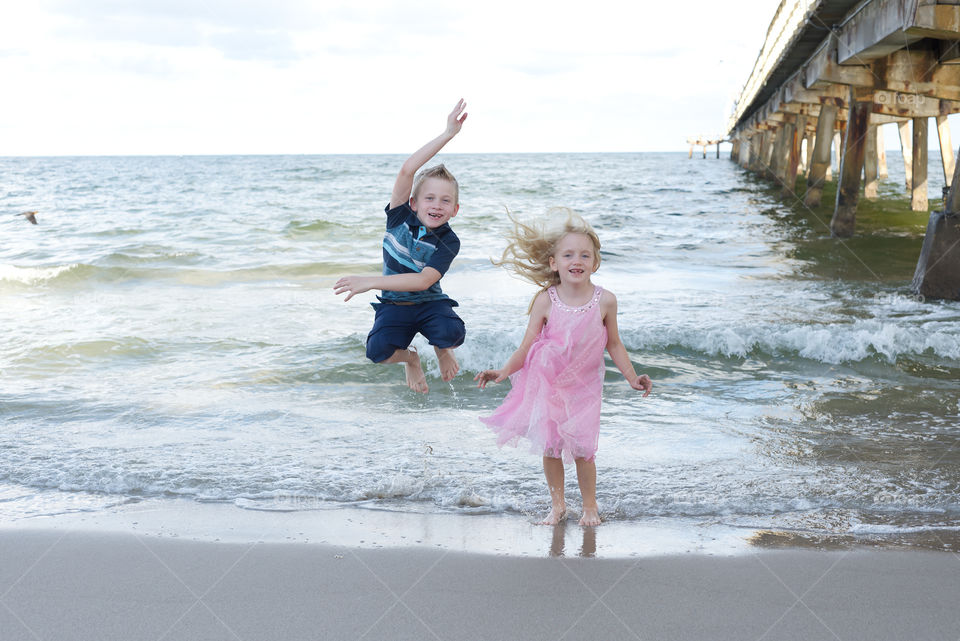 Boy girl twins jumping in the ocean at the beach being silly