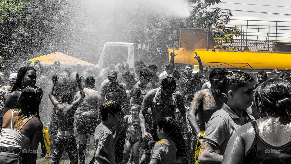 Pessoas tomando banho em festa, muito calor e um caminhão pipa.