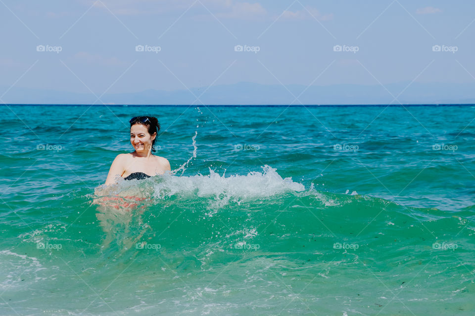 Young woman refreshes and has fun in the sea water on a hot summer day.