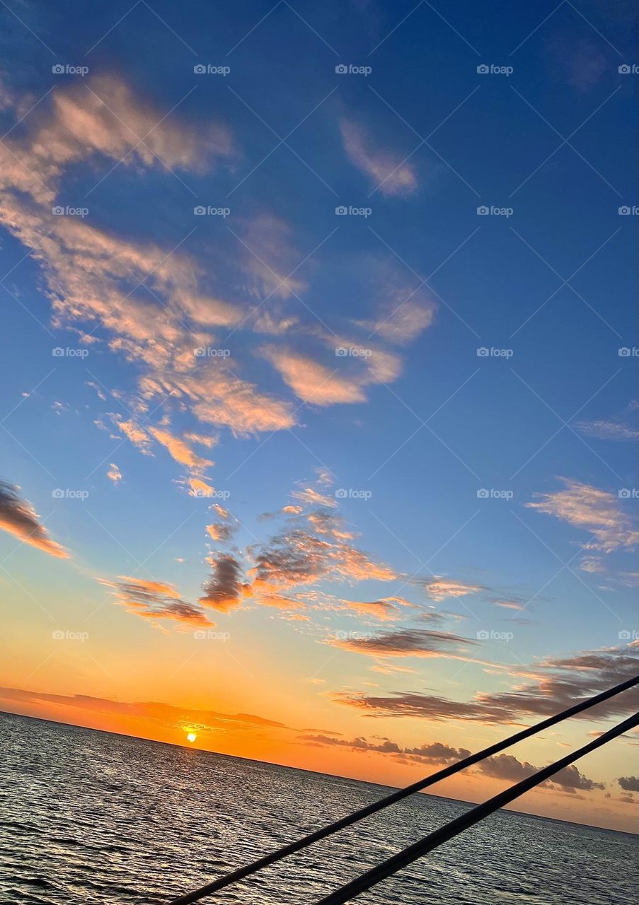 Adrift on a catamaran, the Caribbean sunset paints the sky with hues of gold and purple. The sun dips low, kissing the tranquil sea, while the gentle sway of the vessel syncs with the rhythm of the ocean waves.