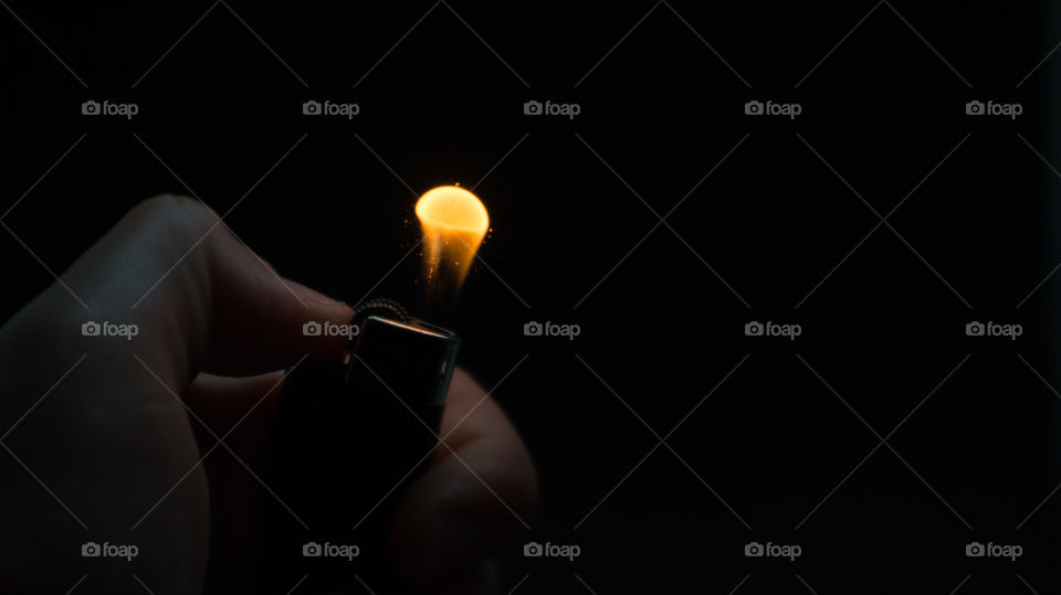 A person has lighters in his hands and he lights it through a flint wheel, the lighter ignites, sparks and fire appear, close-up on a black background.