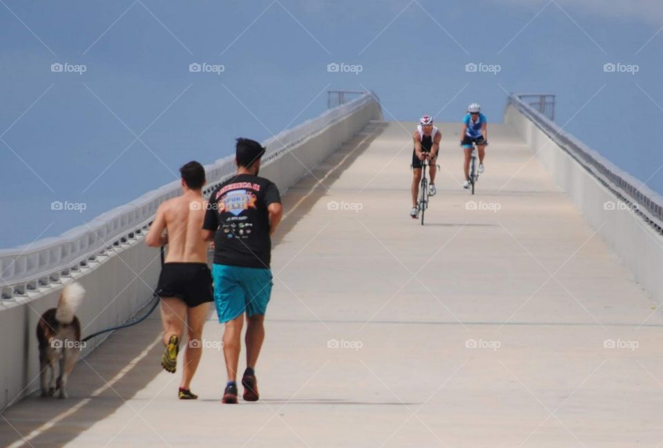 joggers running uphill towards bicyclists heading downhill  on a causeway for pedestrians against a blue sky background