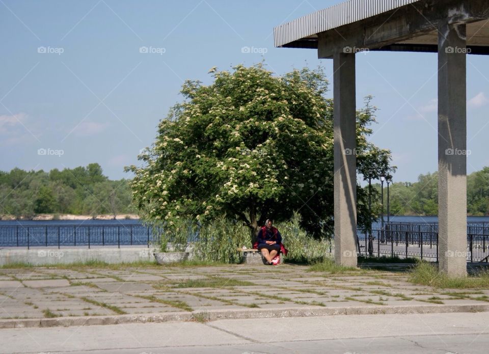 Shelter. Big woman alone under the tree at the river side