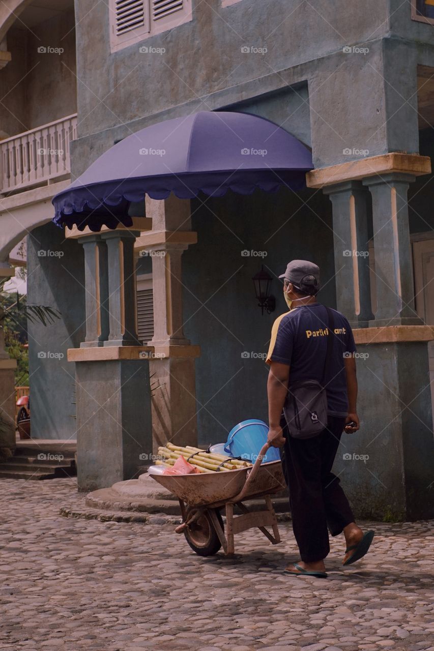 An old man is pushing a cart in front of a blue house