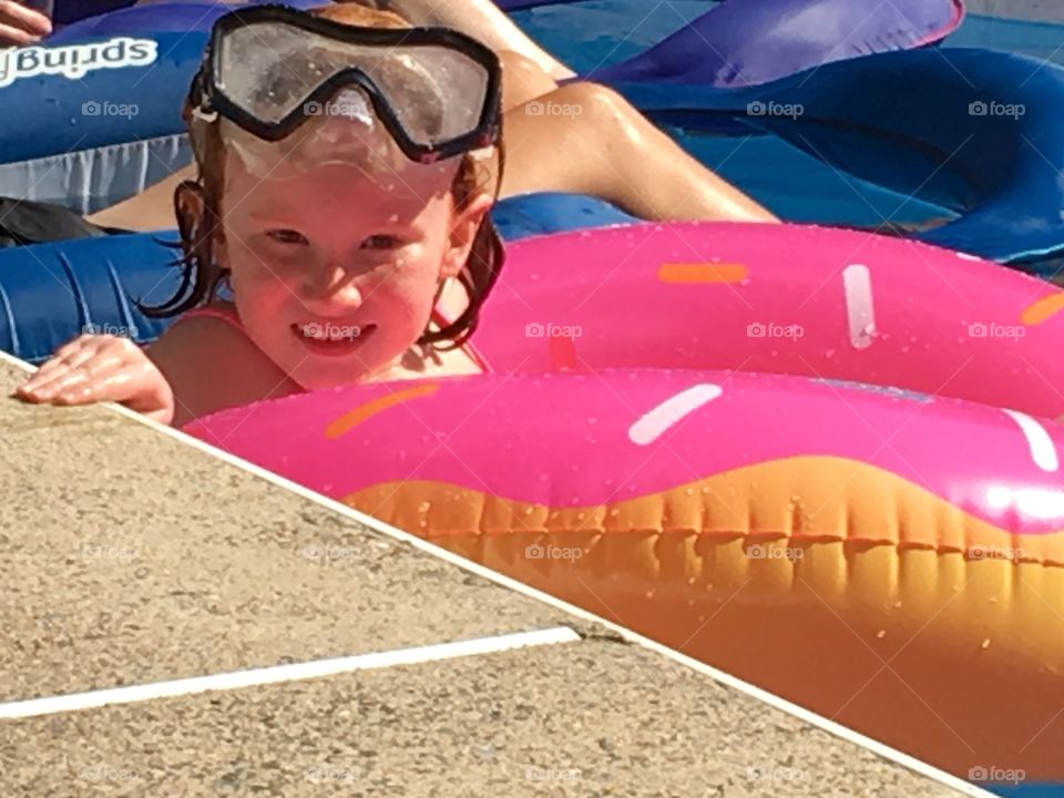 Child in an inflatable ring smiling big and enjoying the pool on a hot summers afternoon.