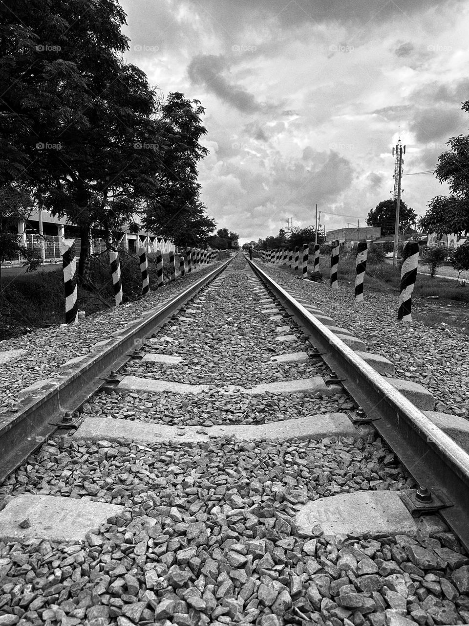 Patterned train tracks with a man walking alone over it to the horizon in a cloudy day