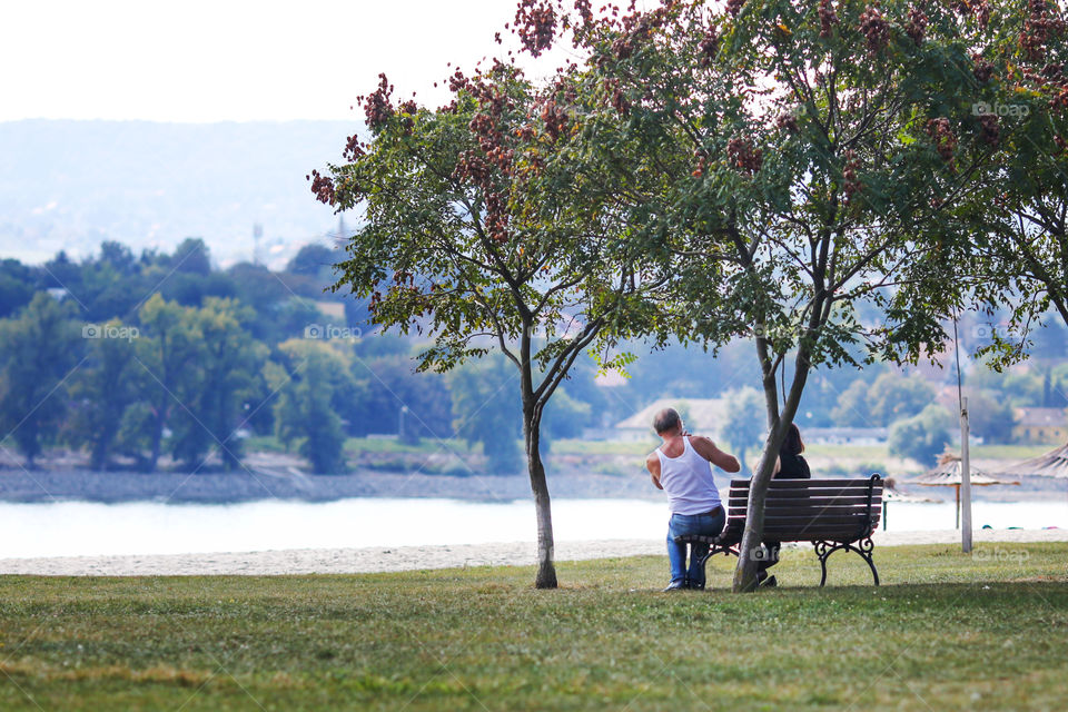 Elder man photigraphing his wife at the bench on the beach