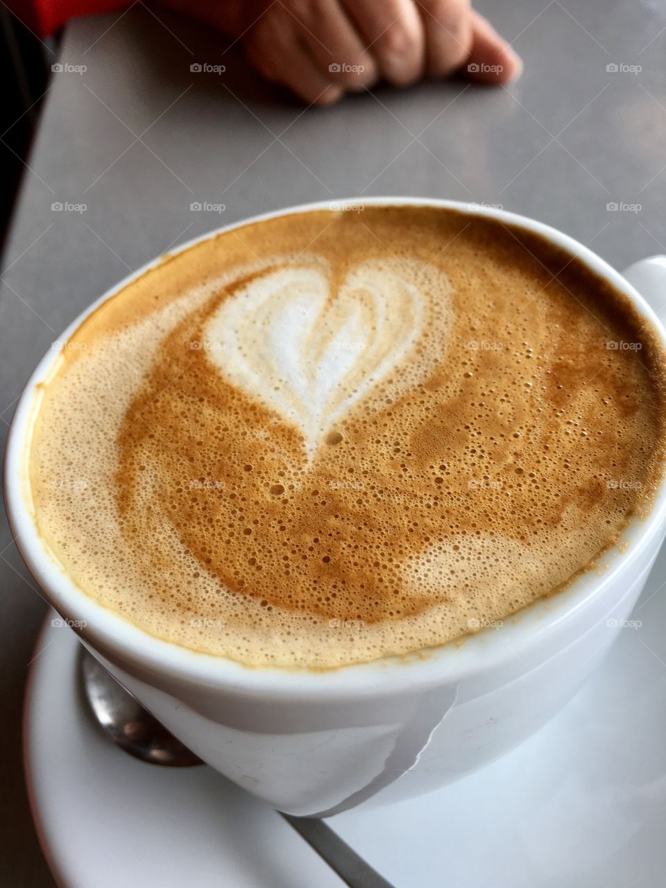 Cafe latte and n white coffee mug and saucer with heart shape formed in cream 