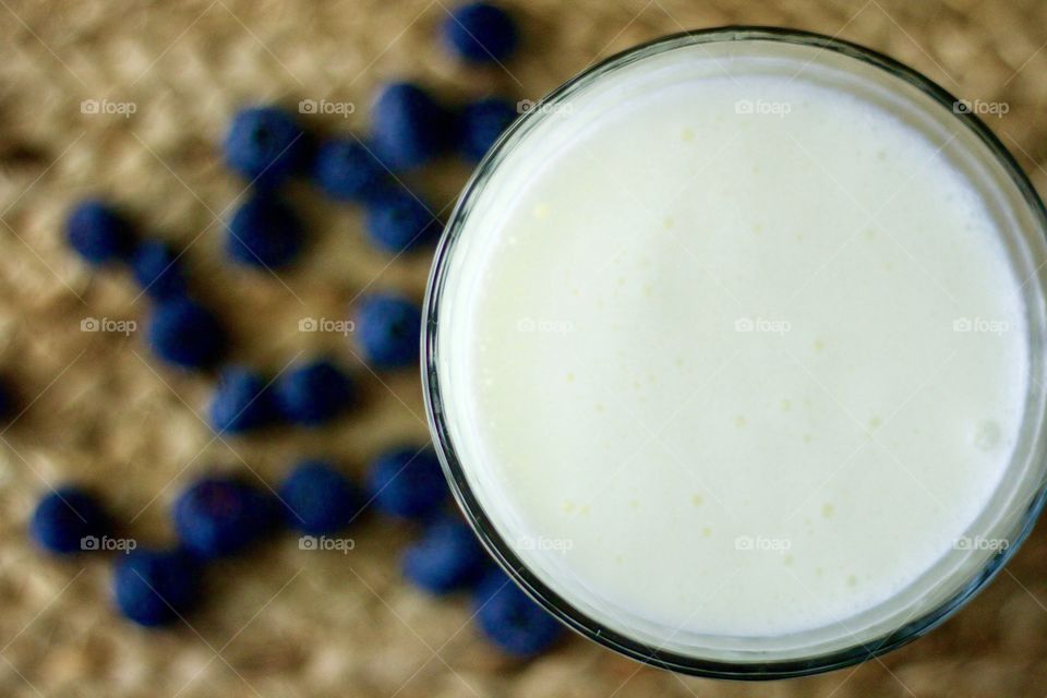 Overhead closeup of dairy kefir with blurred background of blueberries on a natural fiber woven surface