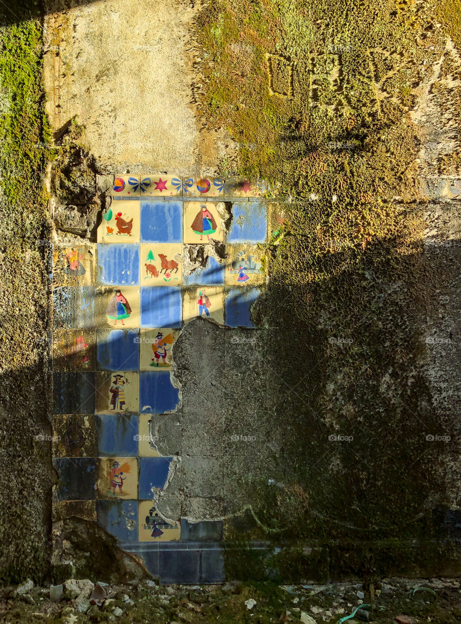 Sunlight hits the few remaining tiles on the wall of an abandoned hotel, the rest of the wall is mossy and graffitied - Portugal 2019