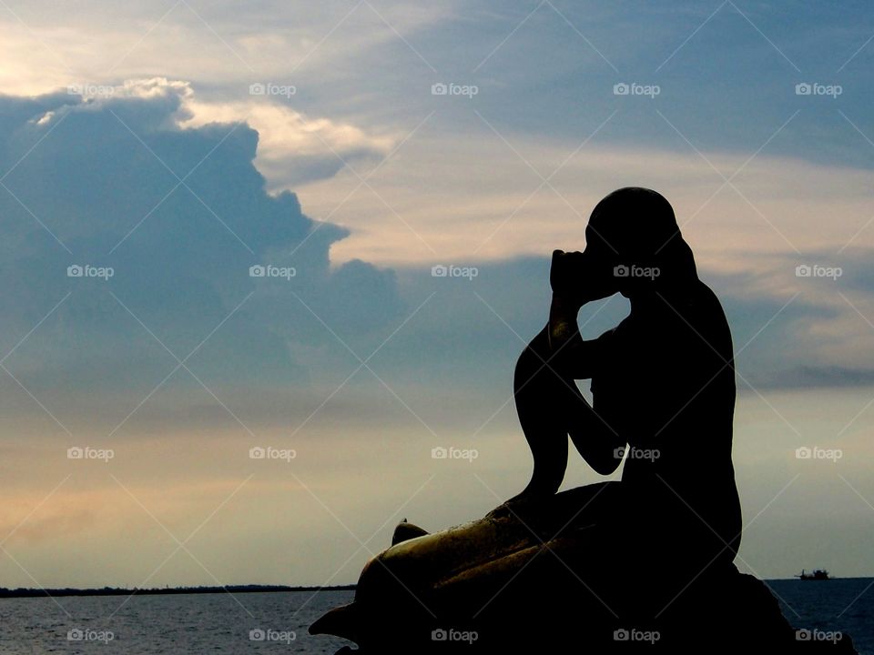 Silhouette mermaid statue at sunset