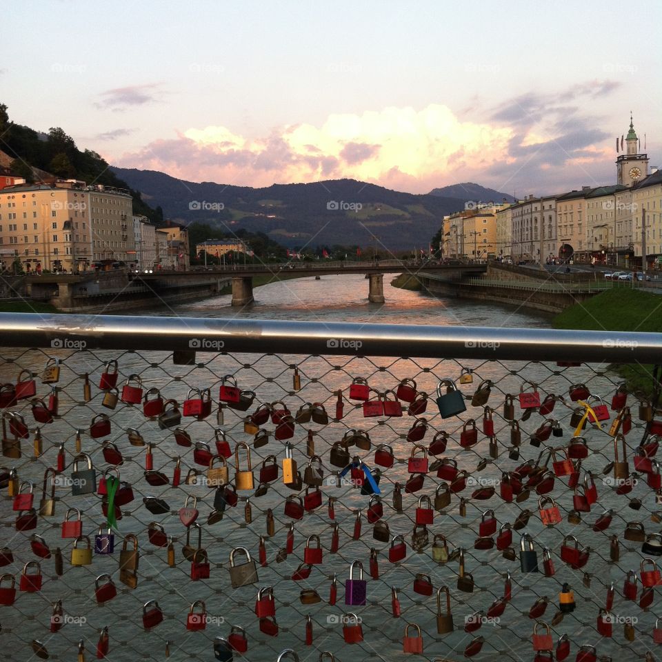 The lock bridge over the Salzach river in Salzburg, Austria. The sun setting behind the mountains, the colorful locks on the bridge symbolizing eternal love