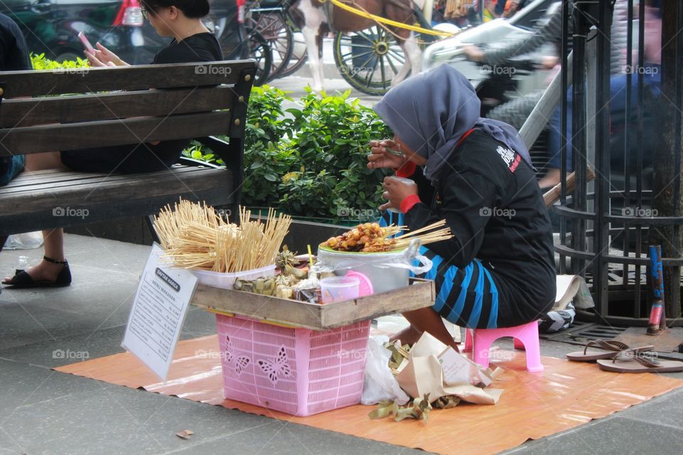 Woman take a rest and eat some food while selling satay on the street at Malioboro Jogja.