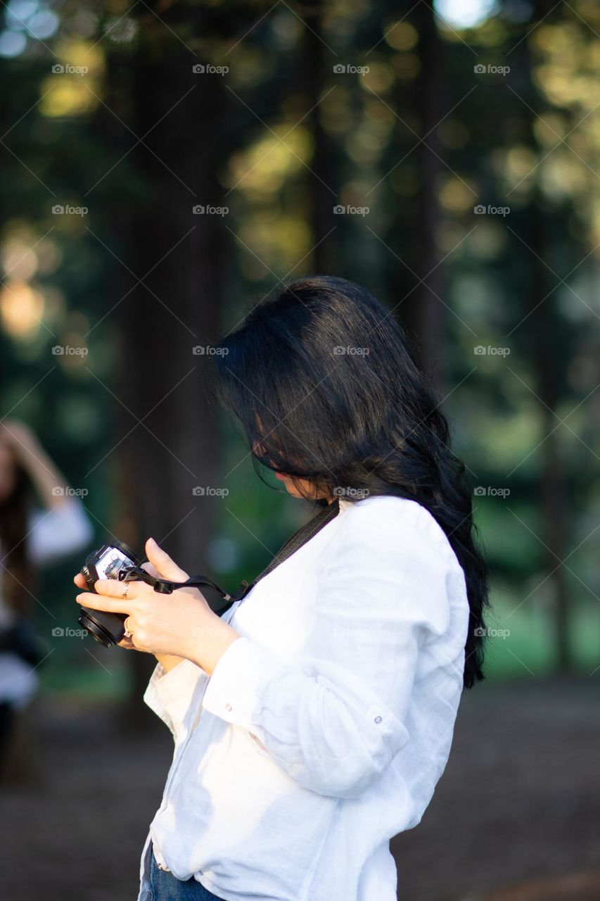 Young woman holding a mirroless camera. Happy young woman backpack and camera photographing outdoors. Healthy hair . Copy space 