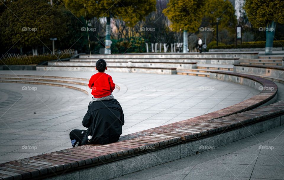 A child is on his father's shoulder while flying a kite .