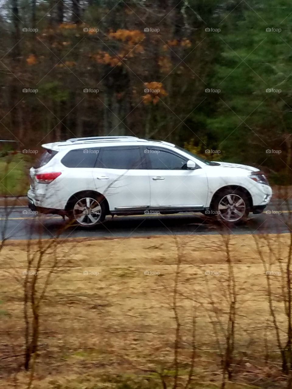 White Nissan Pathfinder SUV driving quickly on road by our house.