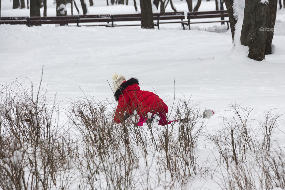 Little girl with red jacket playing and enjoying the snow at the park 
