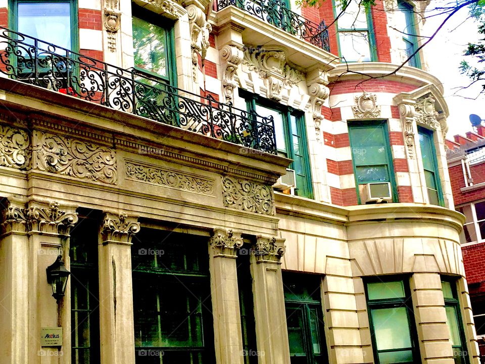 This Fort Greene, Bklyn brownstone.has Greek influence in the ionic columns below the entrance. Balconies have iron cast artful railings. Windows have stucco decorated frames and the striped facade reminds of a Hacienda. 2019. Hypnotic Productions