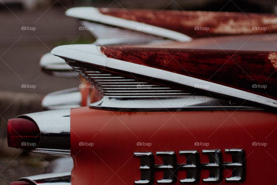 A closeup of the tail end of a red vintage car with an unfinished paint job but original chrome pieces. 