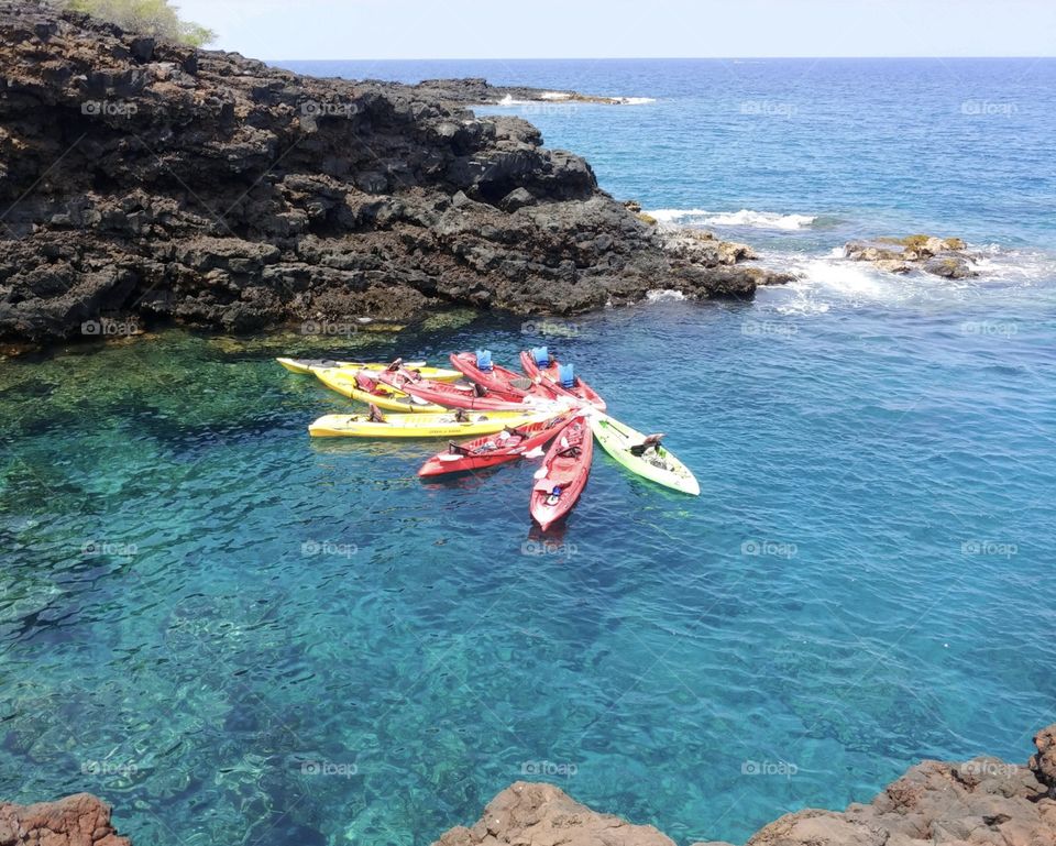 Colorful kayaks floating empty together on clear blue water in a cove created by lava rocks